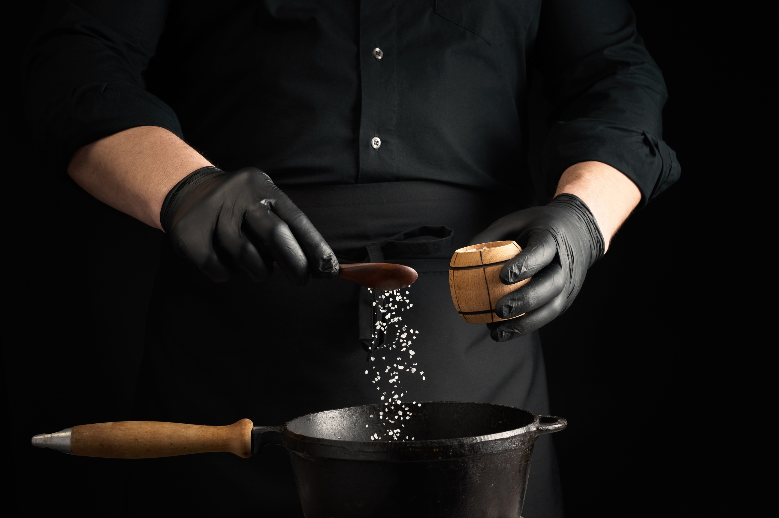 Chef in Black Gloves Puts Salt in a Saucepan